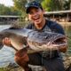 Pemancing berpose bangga dengan lele raksasa hasil tangkapan di kolam Galatama, menunjukkan momen kemenangan dan ketelitian teknik memancing yang sempurna.